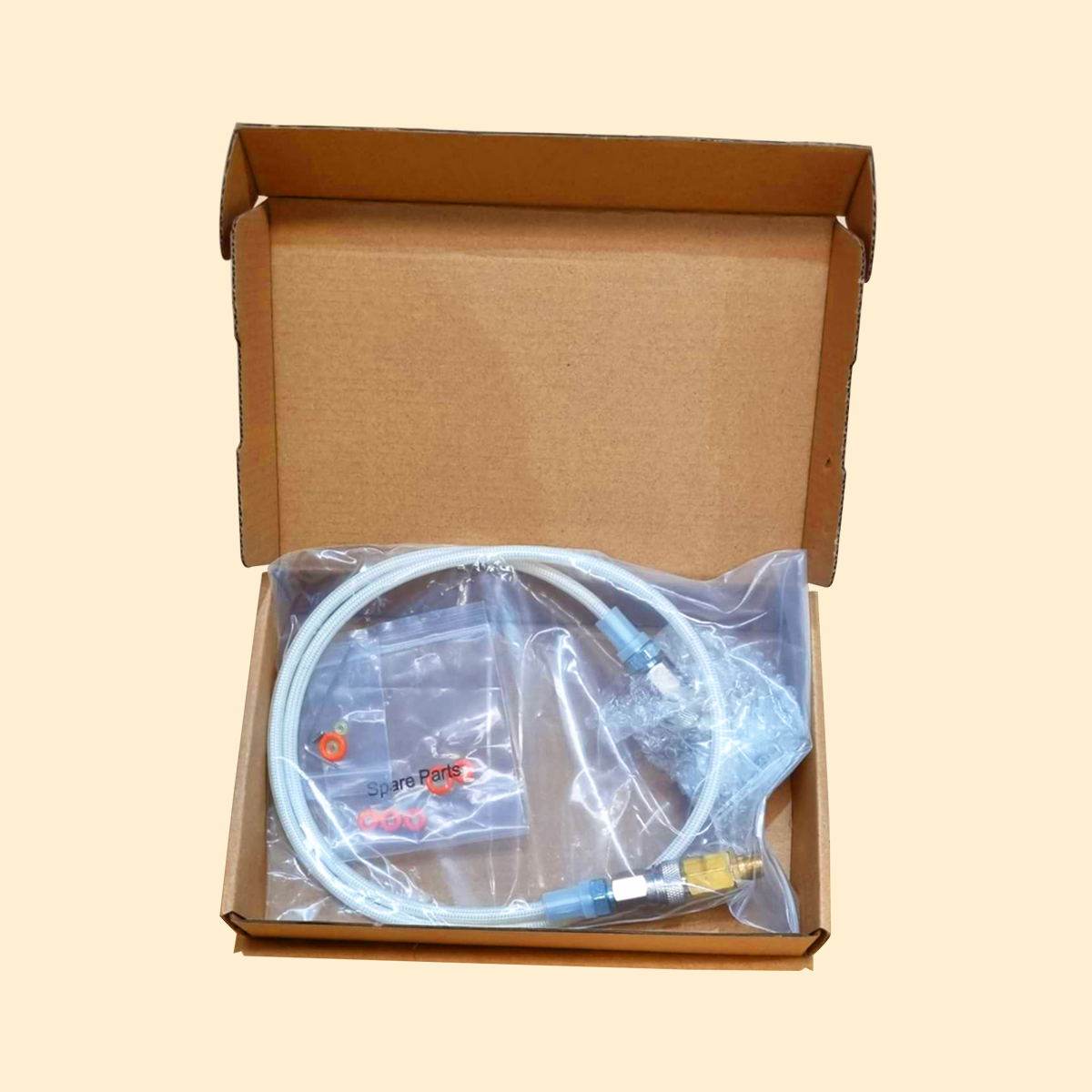 Cardboard box with a clear plastic bag containing a hose and connectors on a beige background